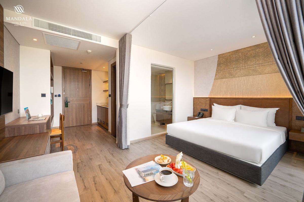A hotel room with a bed, a desk, a chair, a coffee table with breakfast, and a TV.