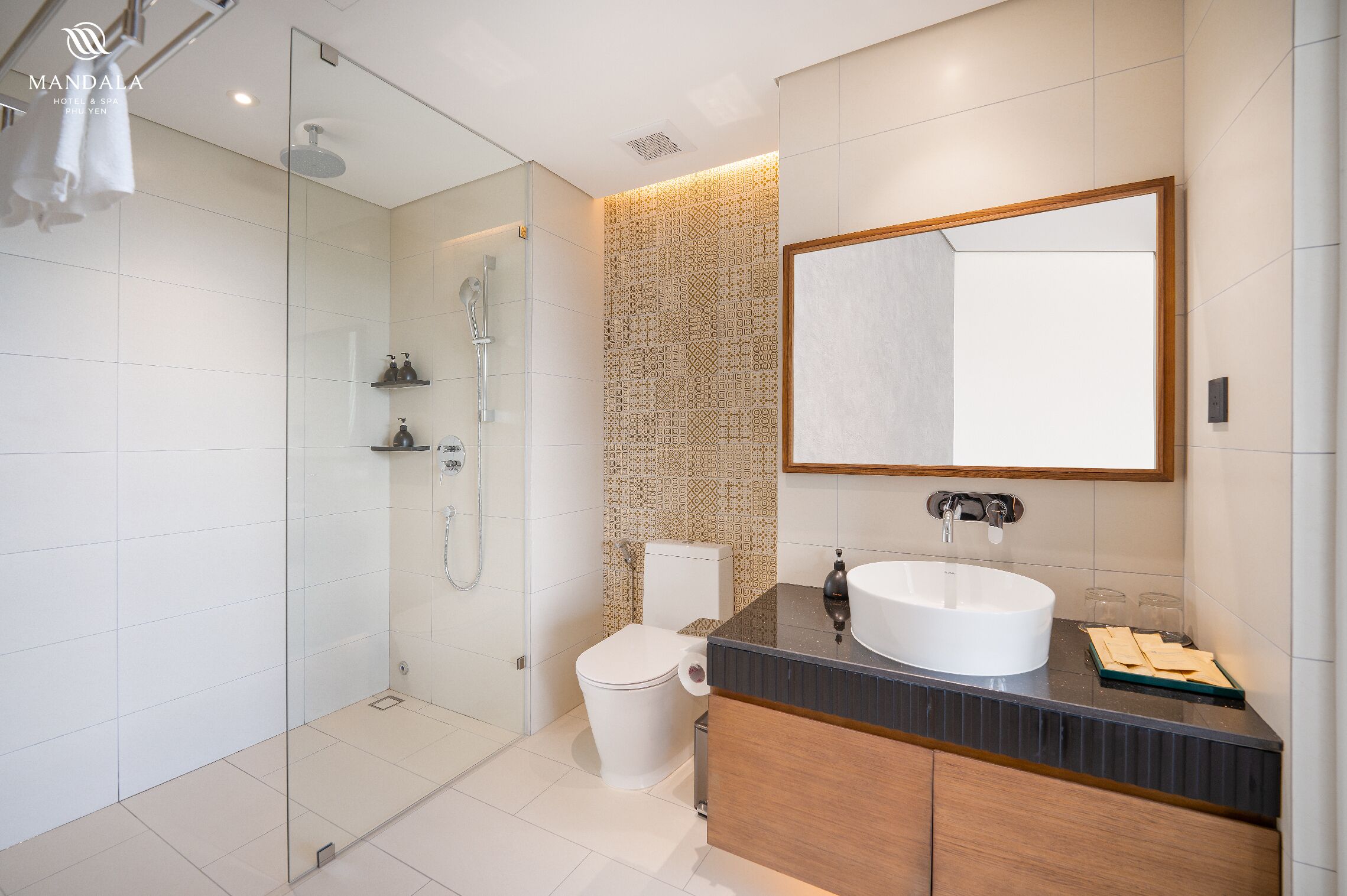 A modern bathroom with a glass shower enclosure, a white toilet, and a large mirror above a black countertop with a white sink.