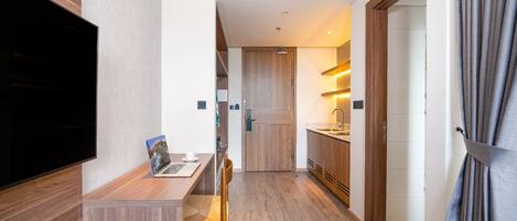 Habitación de hotel moderna con suelo de madera, televisor de pantalla plana, una computadora portátil sobre una mesa de madera y zona de ducha visible a través de una puerta de cristal.