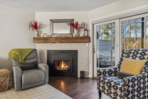 A living room with a fireplace, a sofa, a chair, and a view through a glass door.