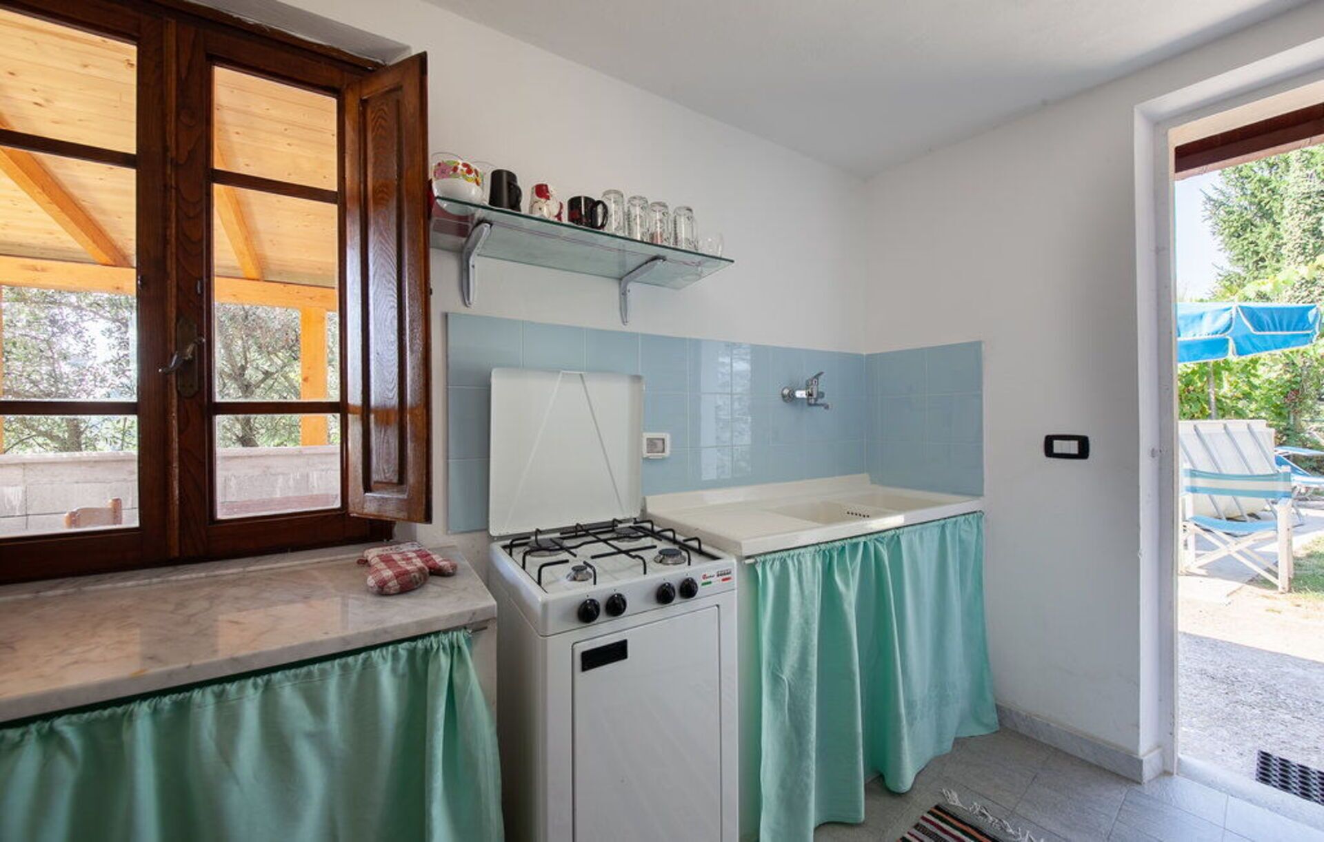 Una cocina compacta con estufa a gas, un lavamanos y una ventana con contraventanas de madera.