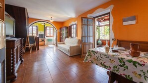 A spacious room with a tiled floor, a sofa, a dining table with a floral tablecloth, and a large window with curtains. - Beautiful private villa with private pool, WIFI, pets allowed and panoramic view, close to Viare... (Gombitelli)