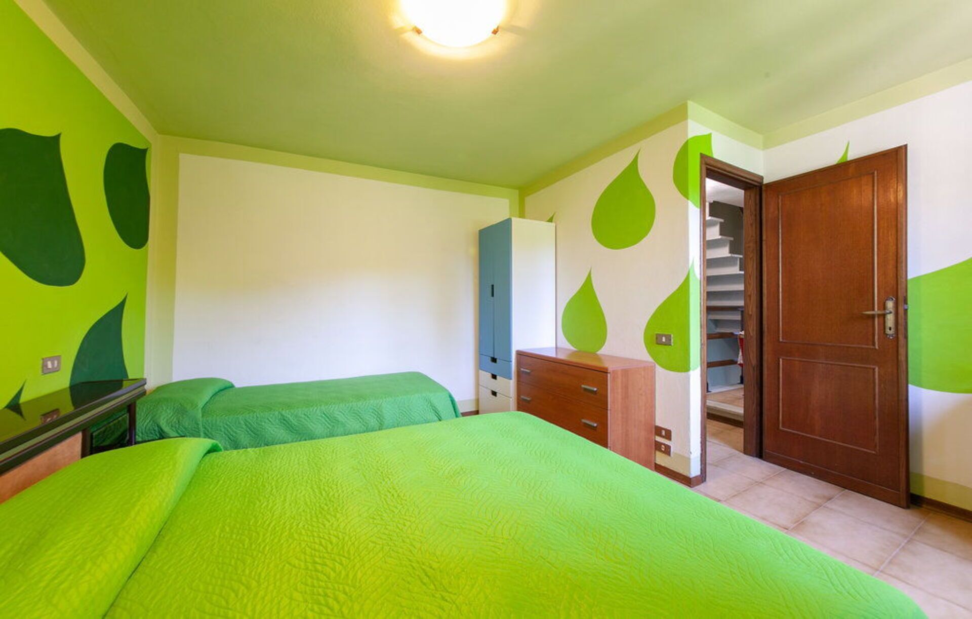 Une chambre avec deux lits, une armoire, un miroir et une porte donnant sur un escalier.