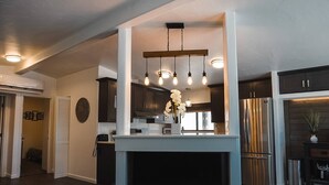 Een moderne keuken met donkere kastjes, een koelkast van roestvrij staal en een centraal eiland met een lamp.