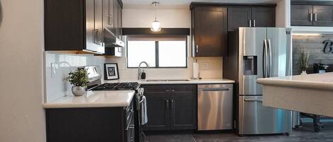 A modern kitchen with dark cabinetry, stainless steel appliances, and a window providing natural light.