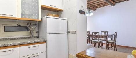Una cocina compacta con gabinetes blancos, un refrigerador empotrado y un comedor con mesa y sillas de madera.