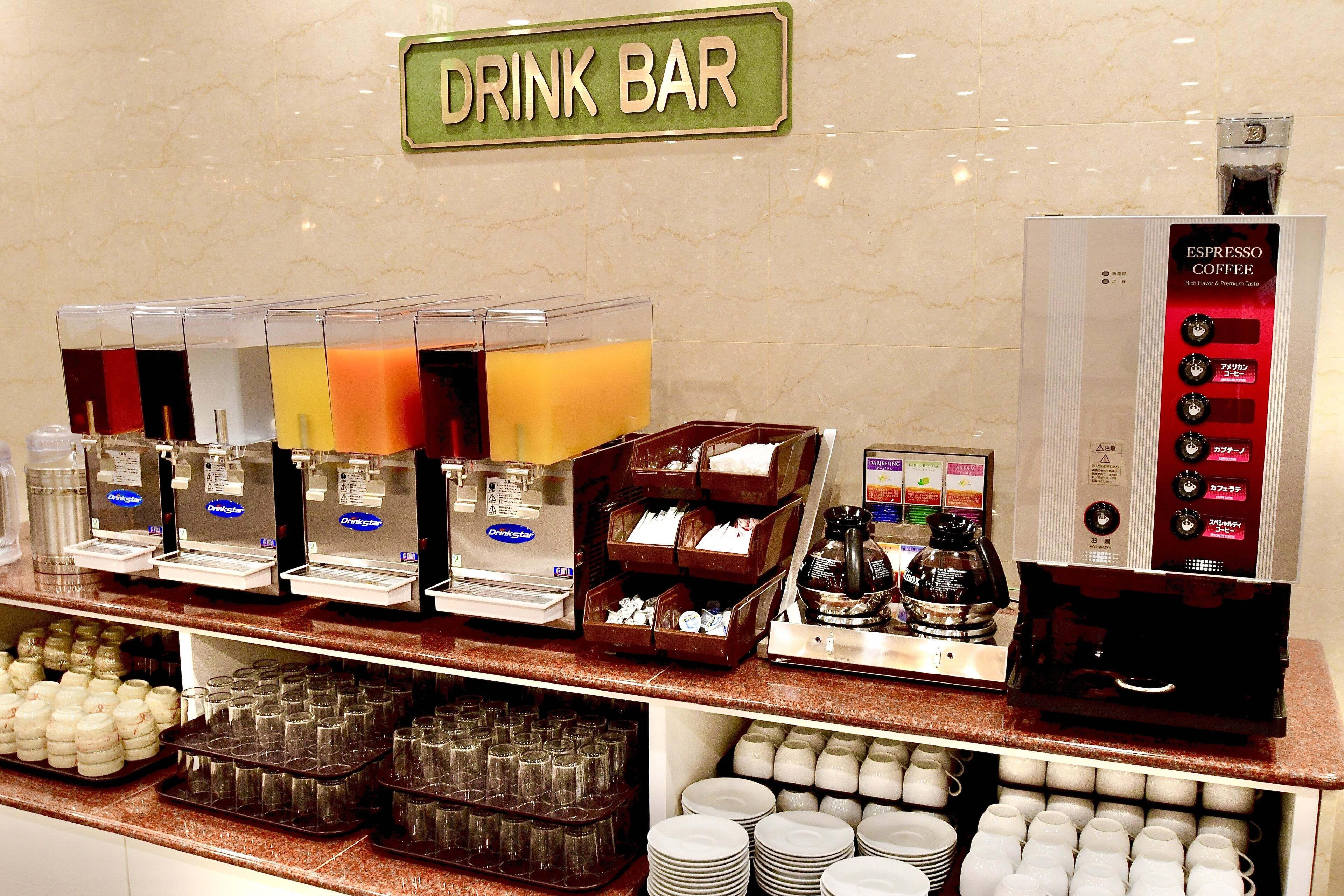 A drink bar with multiple beverage dispensers, coffee machines, and a variety of glassware and cups.