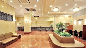 Um saguão de hotel com balcão de recepção, áreas de estar e uma planta decorativa.