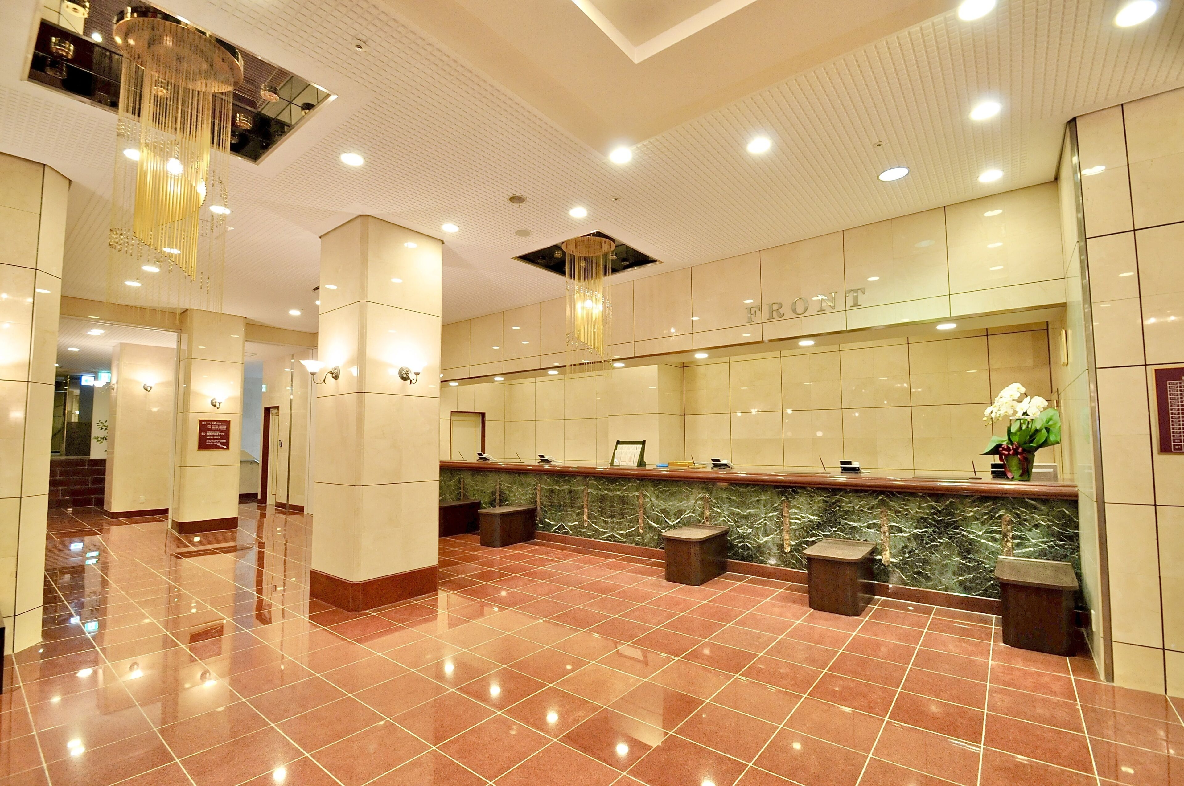 Zona de recepción de un hotel con mostrador de mármol, una araña y suelo pulido.