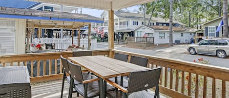 A covered outdoor patio with a wooden table and chairs, overlooking a street with houses and a parked car.