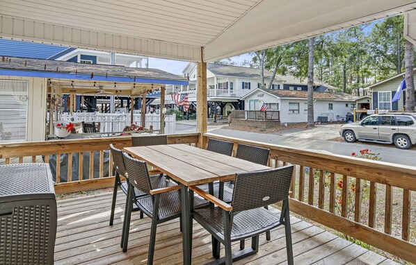 Eine überdachte Terrasse mit Holztisch und -stühlen mit Blick auf eine Straße mit Häusern und einem geparkten Auto.