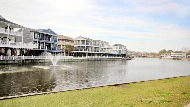 A waterfront property with multiple-story houses, a dock, and a fountain. - The Saltwater Cottage-Golf Cart & Linens Included in Ocean Lakes (Myrtle Beach)