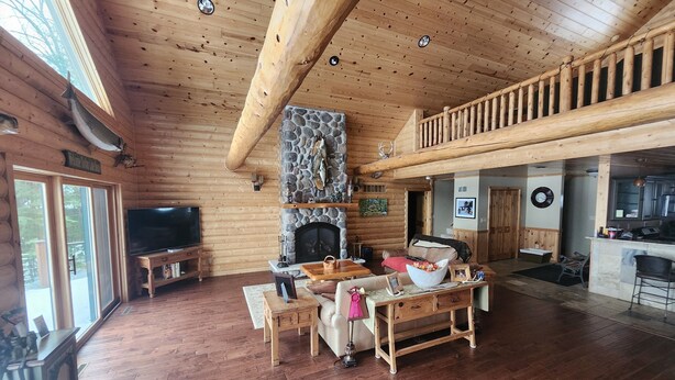 Een ruim houten chalet interieur met een open haard van natuursteen, houten meubels, een televisietoestel en een balkon.