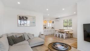 A modern living room with a sofa, a dining area with stools, and a kitchen with pendant lights. - Our Little White House -74  Padman Crescent, Middleton (Middleton)