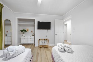 Une chambre d’hôtel avec deux lits, une télévision, un porte-vêtements en bois et un miroir.
