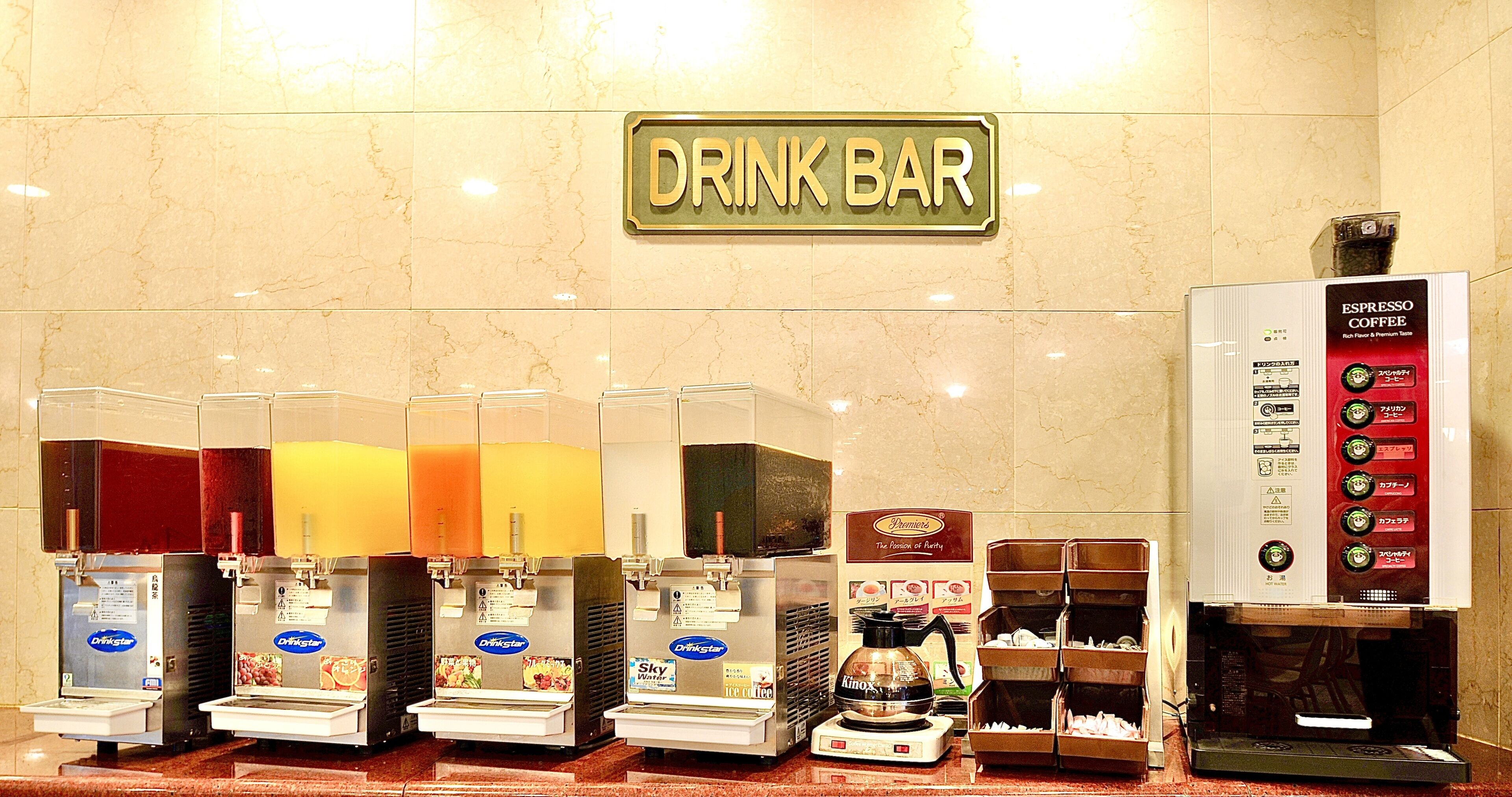 A drink bar with multiple beverage dispensers, a coffee machine, and a sign indicating the location.