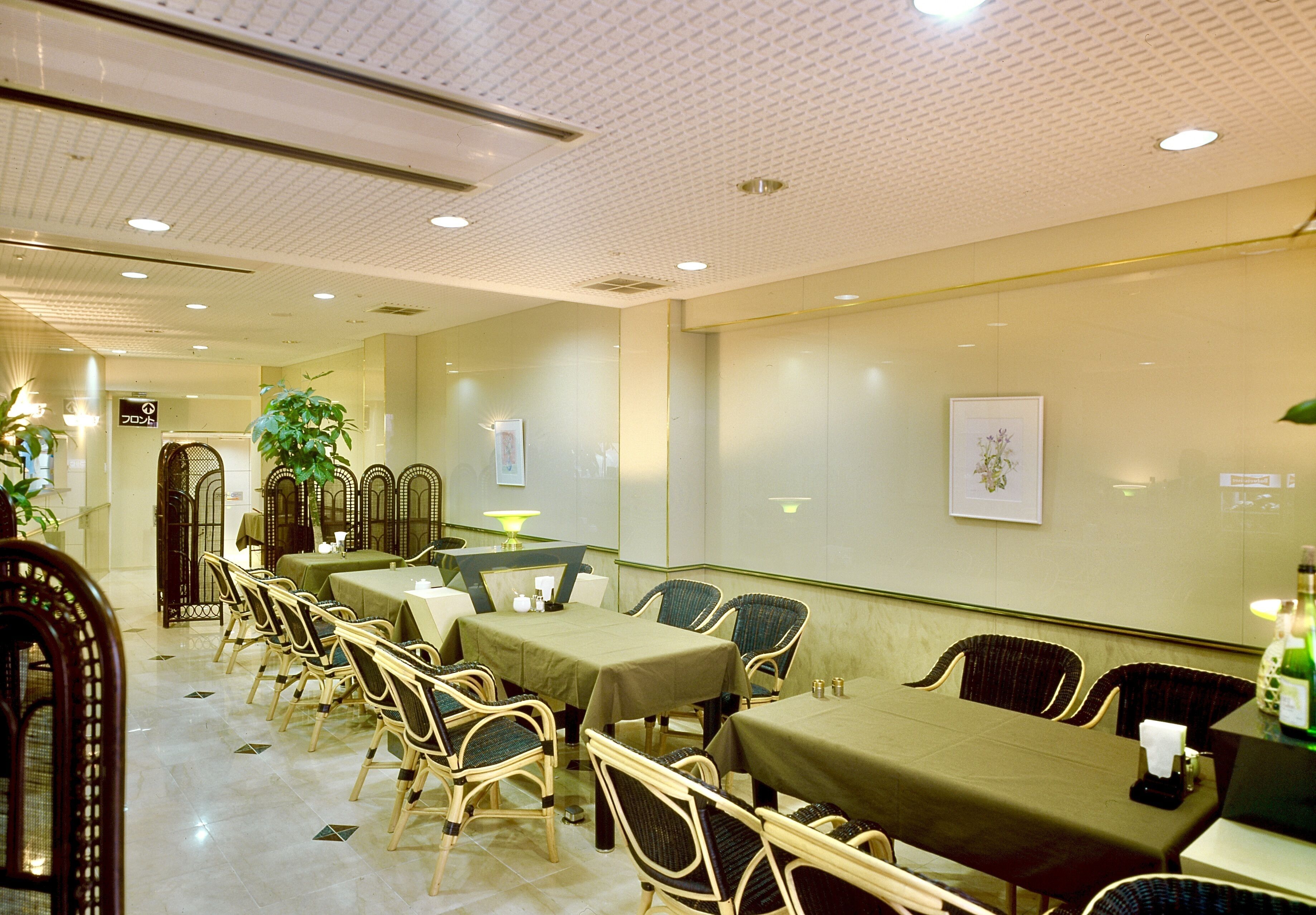 A hotel dining area with multiple tables and chairs, a green tablecloth, and a framed picture on the wall.