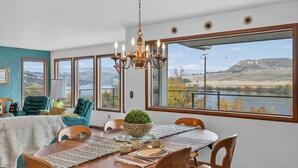 Un espace repas offrant une vue sur un lac et des montagnes, agrémenté d’un lustre et de chaises de couleur turquoise.