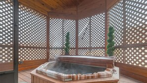 Un bain à remous installé dans un gazebo en bois, doté de murs en treillis et d’un plancher en bois.