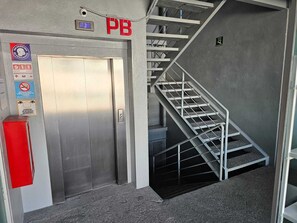 Un ascenseur doté de panneaux d’indication pour les situations d’urgence, une cage d’escalier et un extincteur rouge.
