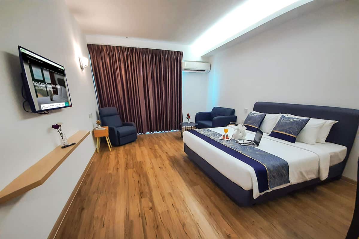 Ein Hotelzimmer mit einem großen Bett, zwei Sesseln, einem kleinen Tisch, einem Fernseher und einem Fenster mit Vorhängen.