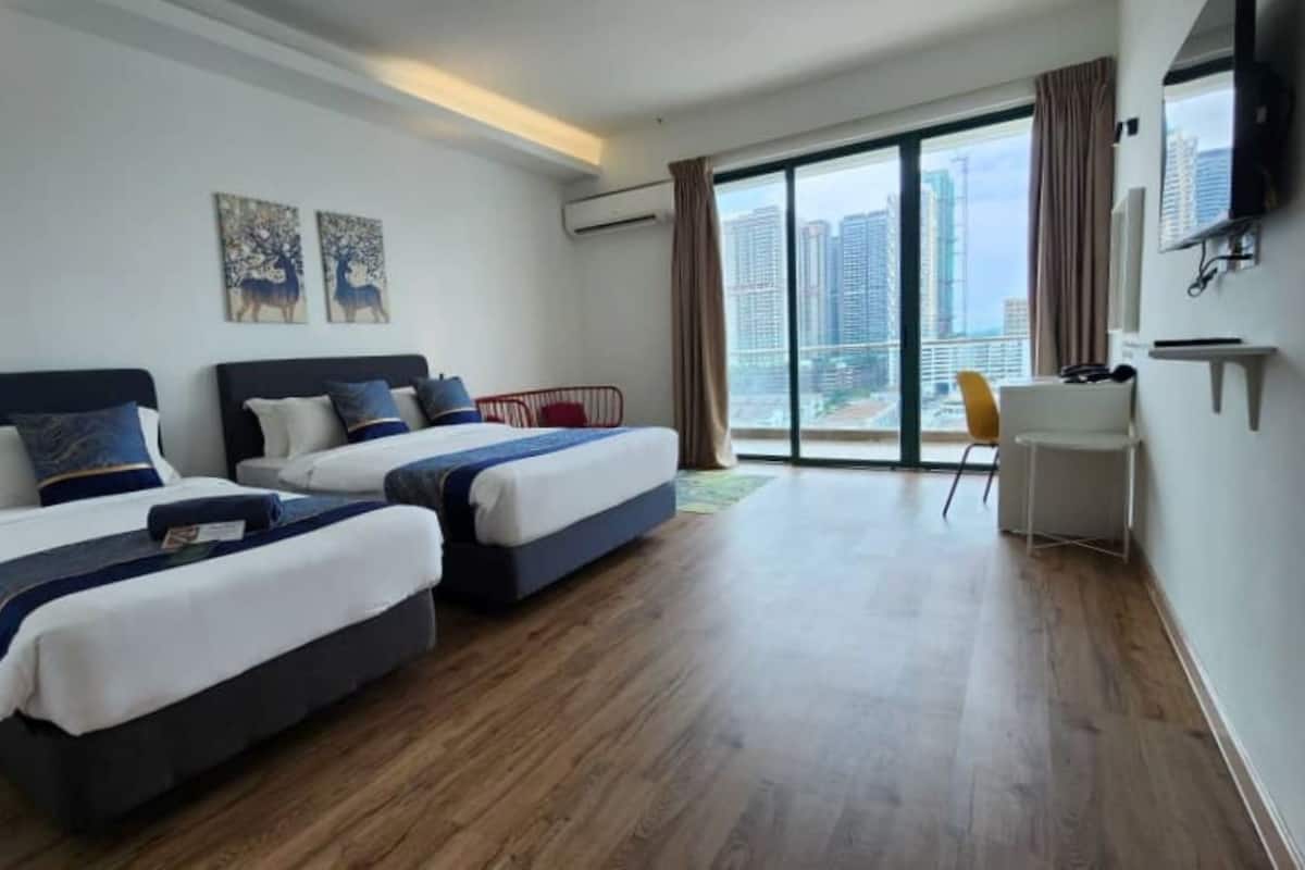 Ein Hotelzimmer mit zwei Betten, einem großen Fenster mit Blick auf die Stadt, einem Flachbildfernseher und einer kleinen Schreibtischzeile.