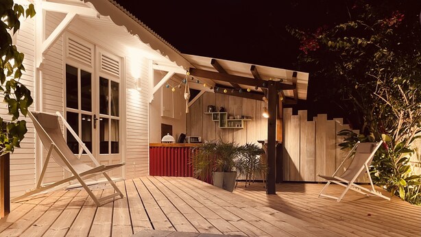 Een houten terras met een zwembad, twee ligstoelen en een overdekt gedeelte met een kookgedeelte.