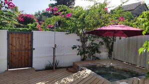 Een houten terras met een jacuzzi, omringd door een witte muur en weelderige begroeiing.