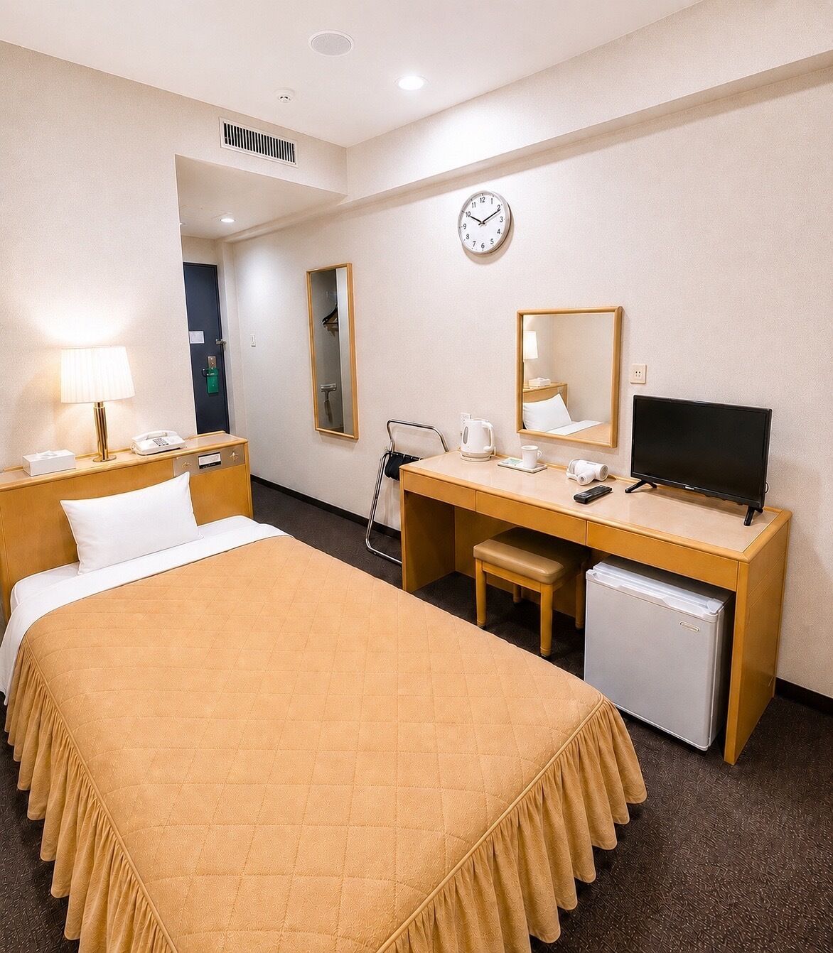 Een hotelkamer met een bed, bureau, stoel en een kleine koelkast.