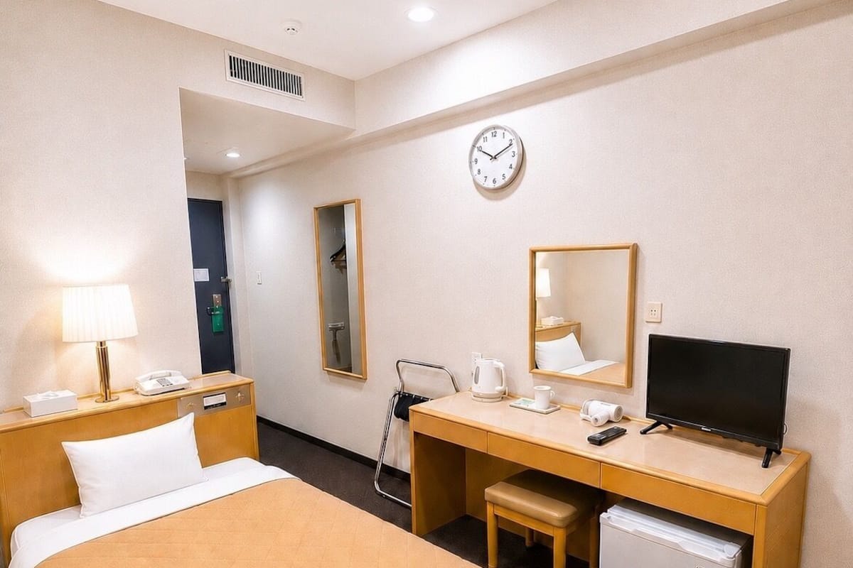 Habitación de hotel con cama, escritorio, silla y un refrigerador pequeño.