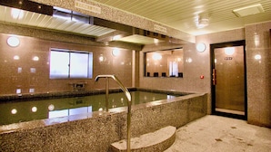Una zona de piscina con escalones que bajan al agua, un espejo que refleja la habitación y una puerta con el rótulo "SAWARA".