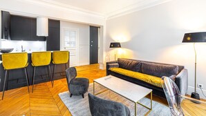 Moderni olohuone, jossa on sohva, nojatuoleja, sohvapöytä ja keittiöalue, jossa on baarituoleja.