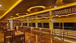 A restaurant with wooden furniture, a fan, and a patterned ceiling. - Royal Houseboats (Ambalapuzha)