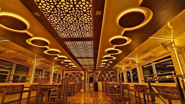 L’intérieur d’un train, avec des luminaires circulaires, des panneaux de bois et un plafond orné de motifs.