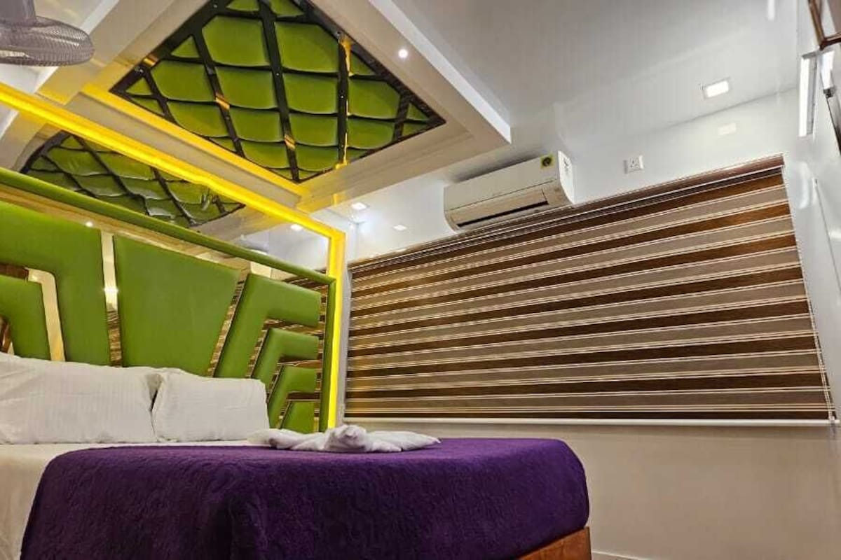 Une chambre à coucher moderne avec une tête de lit verte, une couvre-lit violette et une lucarne au-dessus du lit.