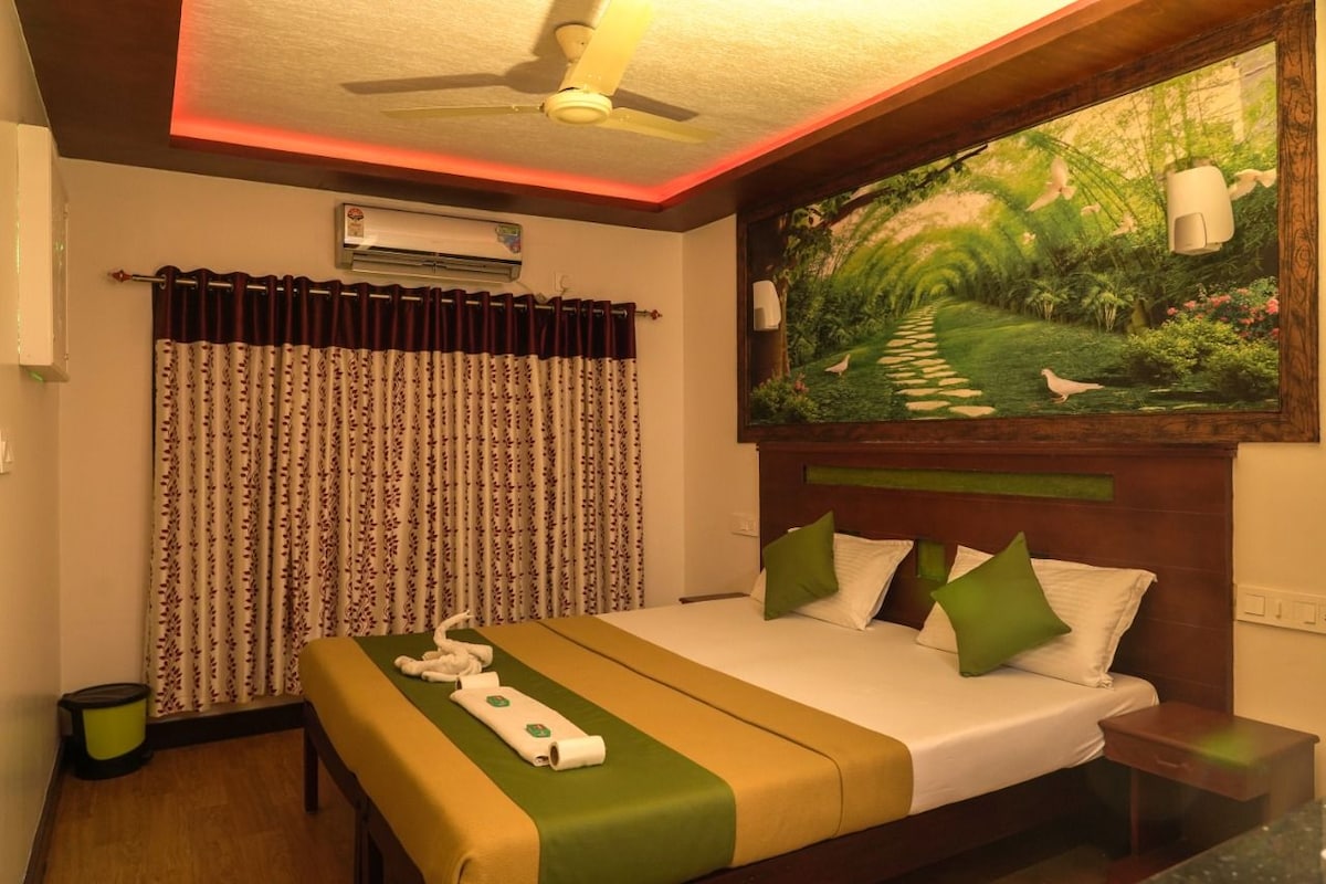 Une chambre d’hôtel avec un lit, un tableau représentant un jardin, un ventilateur de plafond et une fenêtre avec des rideaux.