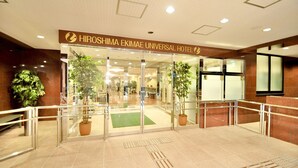 La entrada al Hotel Universal Hiroshima Ekimae, con puertas de vidrio, plantas en macetas y piso de baldosas.