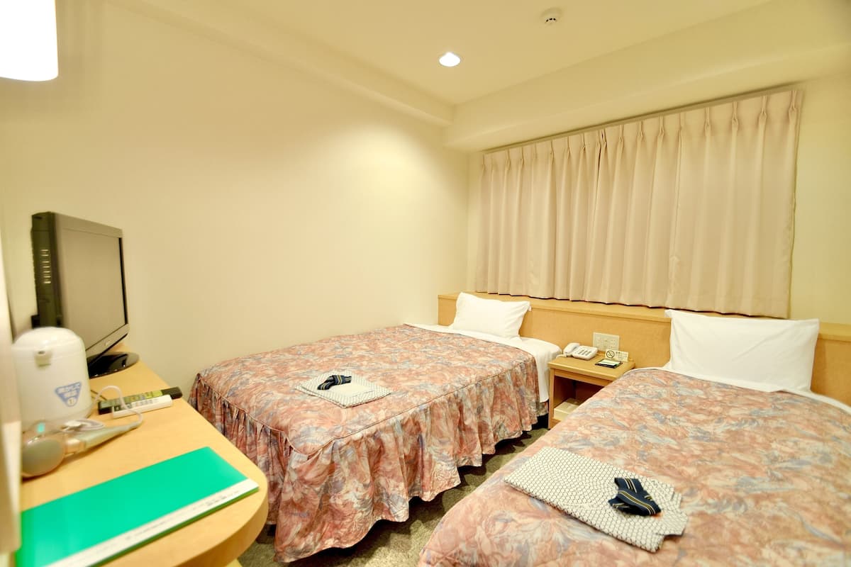 Ein Hotelzimmer mit zwei Betten, einem Schreibtisch mit Computer, Telefon und Fernseher.