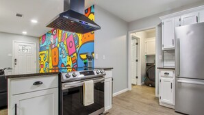 A kitchen with a modern stove, white cabinets, and a colorful abstract mural on the wall.