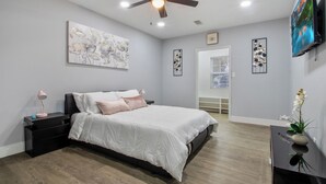 A modern bedroom with a bed, nightstands, a ceiling fan, artwork, and a TV.
