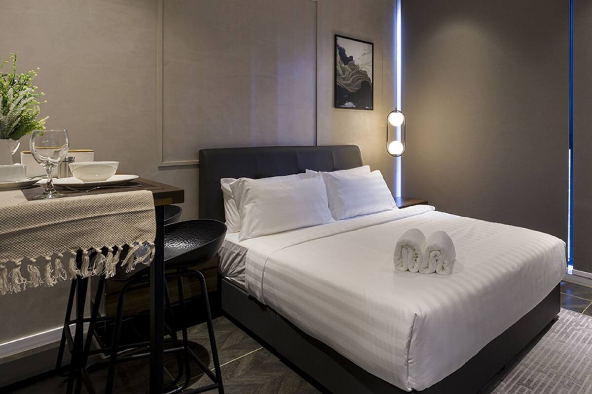 Una habitación de hotel con una cama bien hecha, un pequeño escritorio con una planta y un taburete.