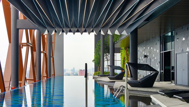 An indoor infinity pool with a city view, modern architecture, and lounge chairs.