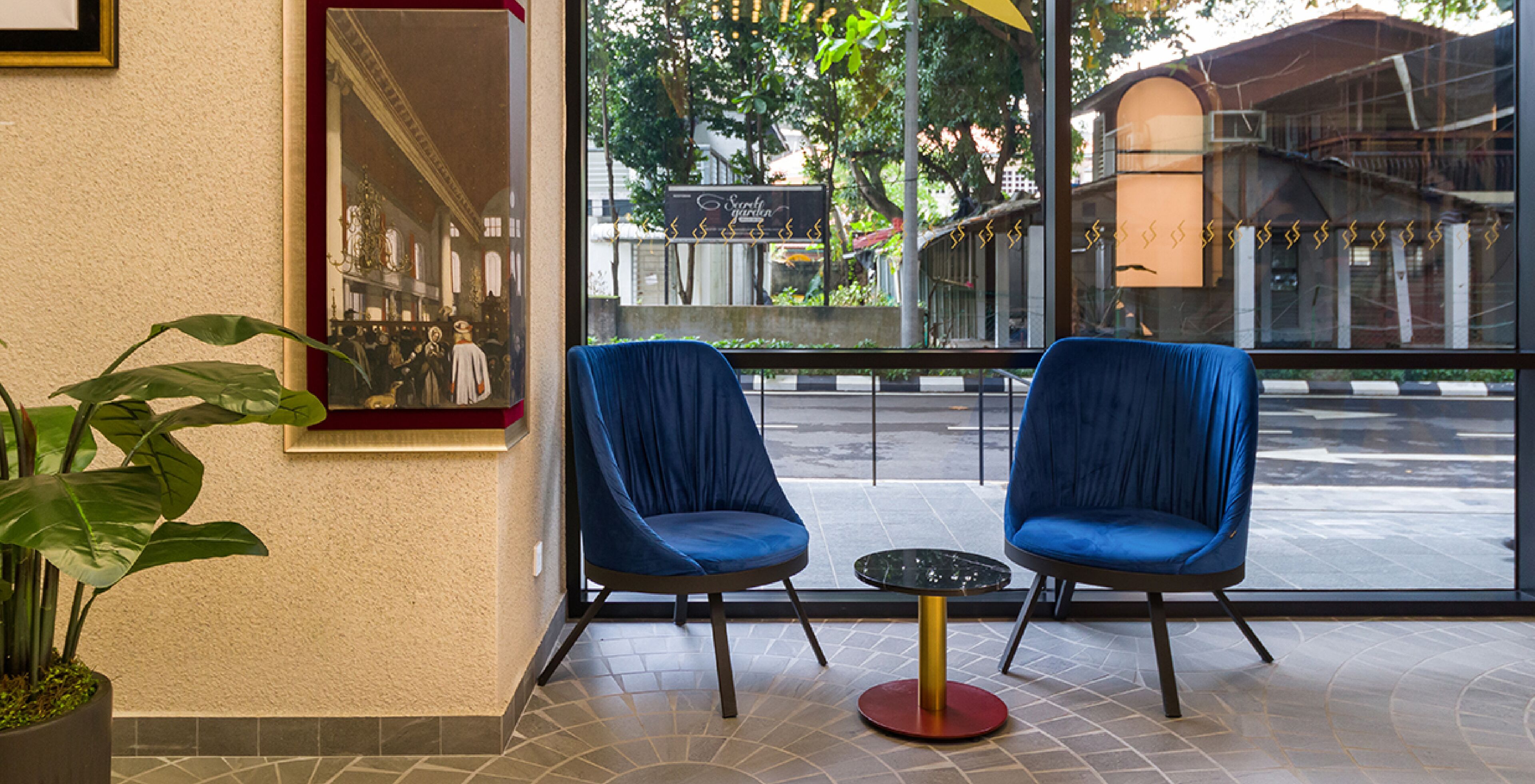 A seating area with two blue chairs and a small table, a potted plant, and a mirror on the wall.