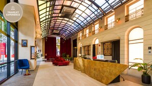 A spacious lobby with a high ceiling, a reception desk, seating areas, and large windows allowing natural light.