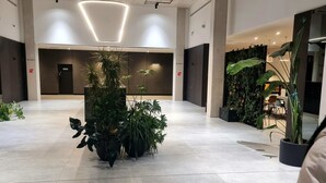 Eine geräumige Lobby mit einer zentralen Pflanzengestaltung, einer hohen Decke mit eingelassener Beleuchtung und einer modernen Wand mit vertikalem Garten.