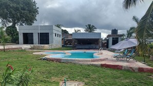 Una piscina con borde de piedra, rodeada de césped y algunas palmeras.