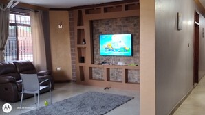 Una sala de estar con televisor, sofá de cuero y alfombra gris.