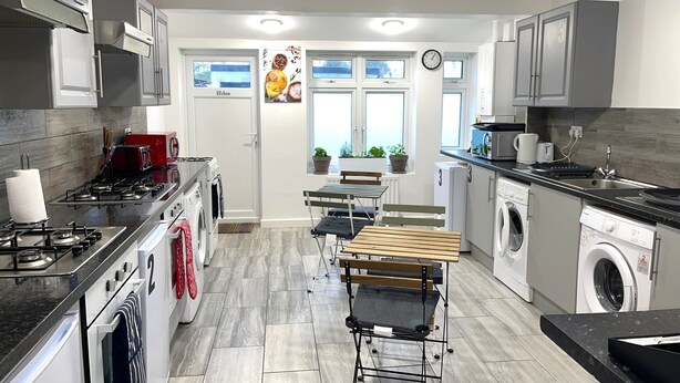Una cocina moderna con estufa a gas, horno, microondas y lavadora integrada. Cuenta con un comedor con mesa y sillas, y una ventana con vistas al exterior.