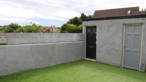 Un patio trasero cercado con césped artificial, un muro de concreto y una puerta.