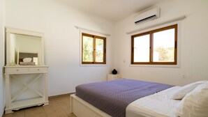 A bedroom with a bed, a nightstand, a dresser, and two windows. - Captivating 2-Bed House (Larnaca Agios Theodoros)